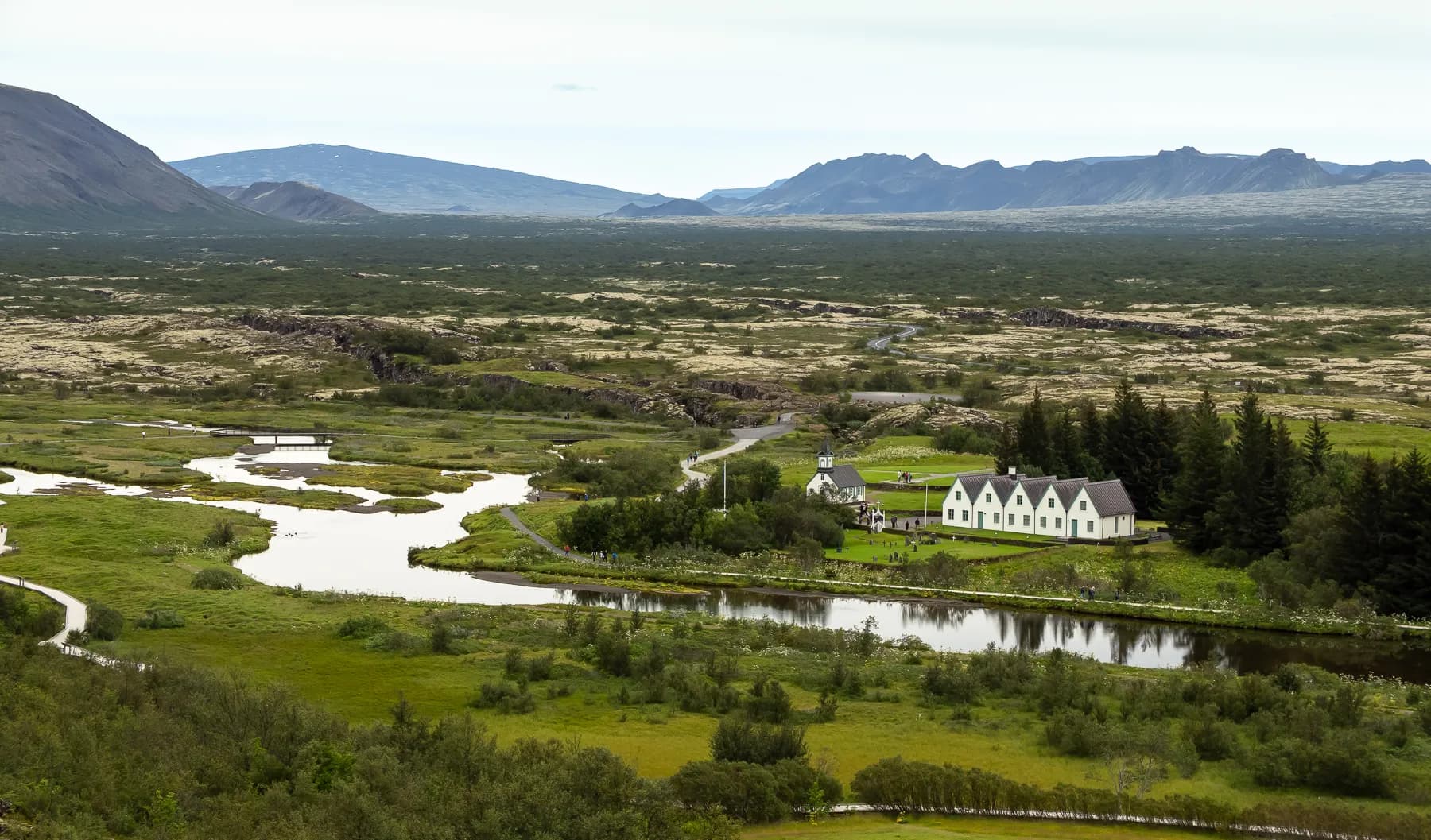 Wide view of green fields, low stone walls, and distant hills in Þingvellir National Park, Iceland.
