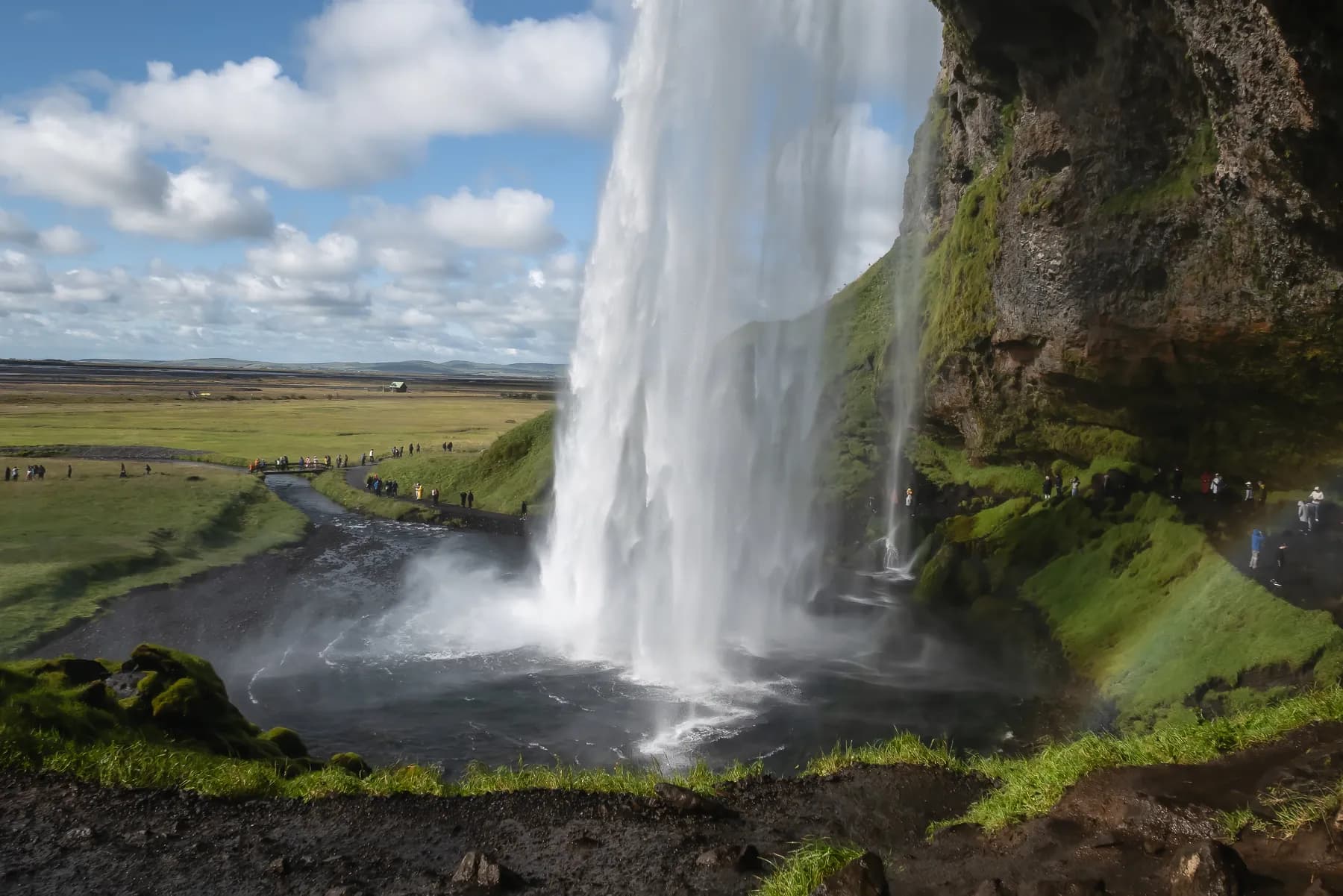 Seljalandsfoss waterfall with bright skies, clouds, and green fields